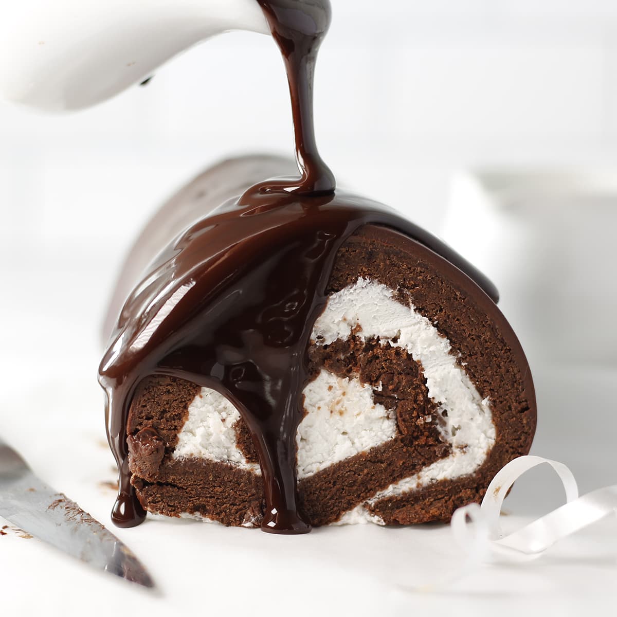 Rolle cake with whipped cream inside and a ganache being poured.