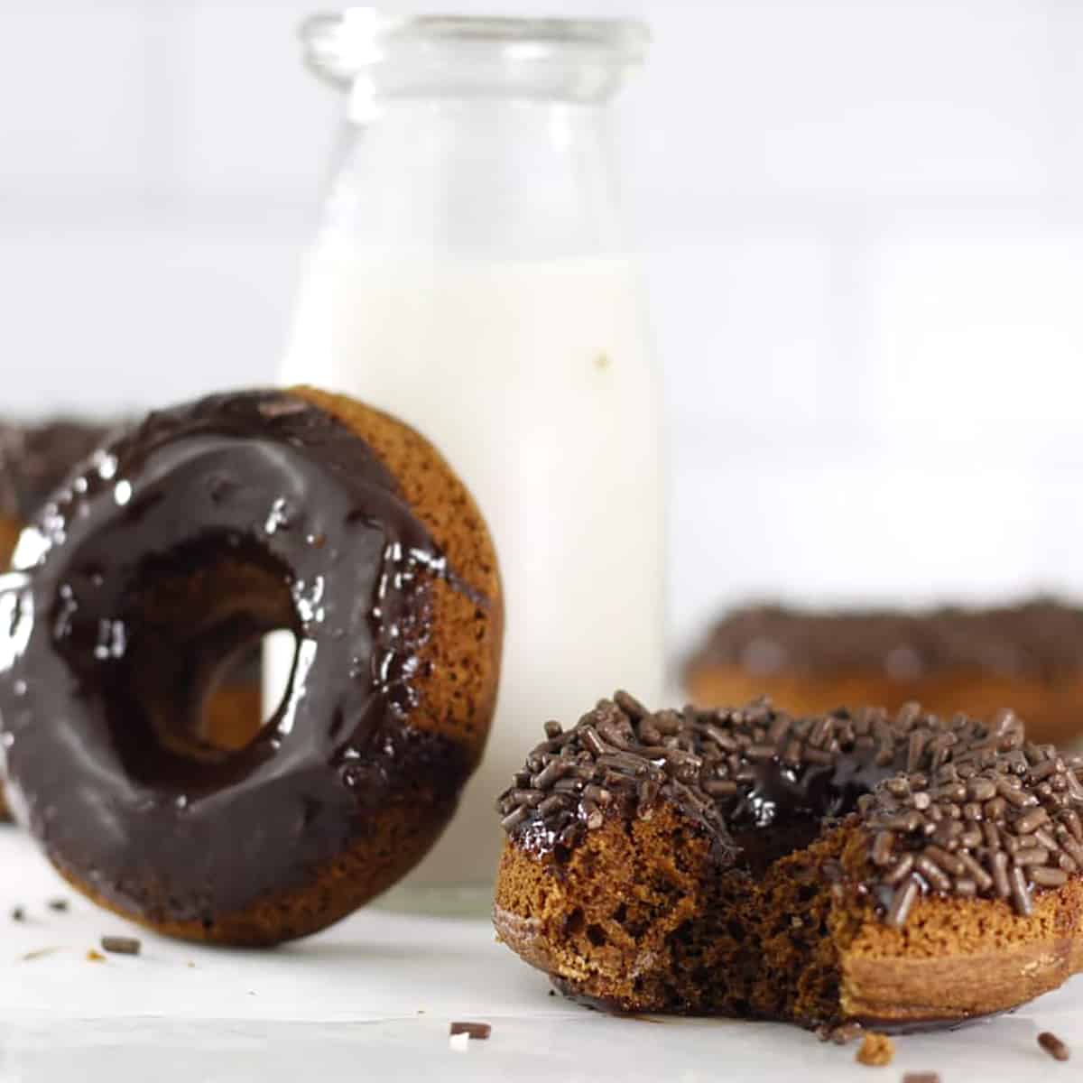 a chocolate frosted donut leaning on a milk bottle and another with a bite