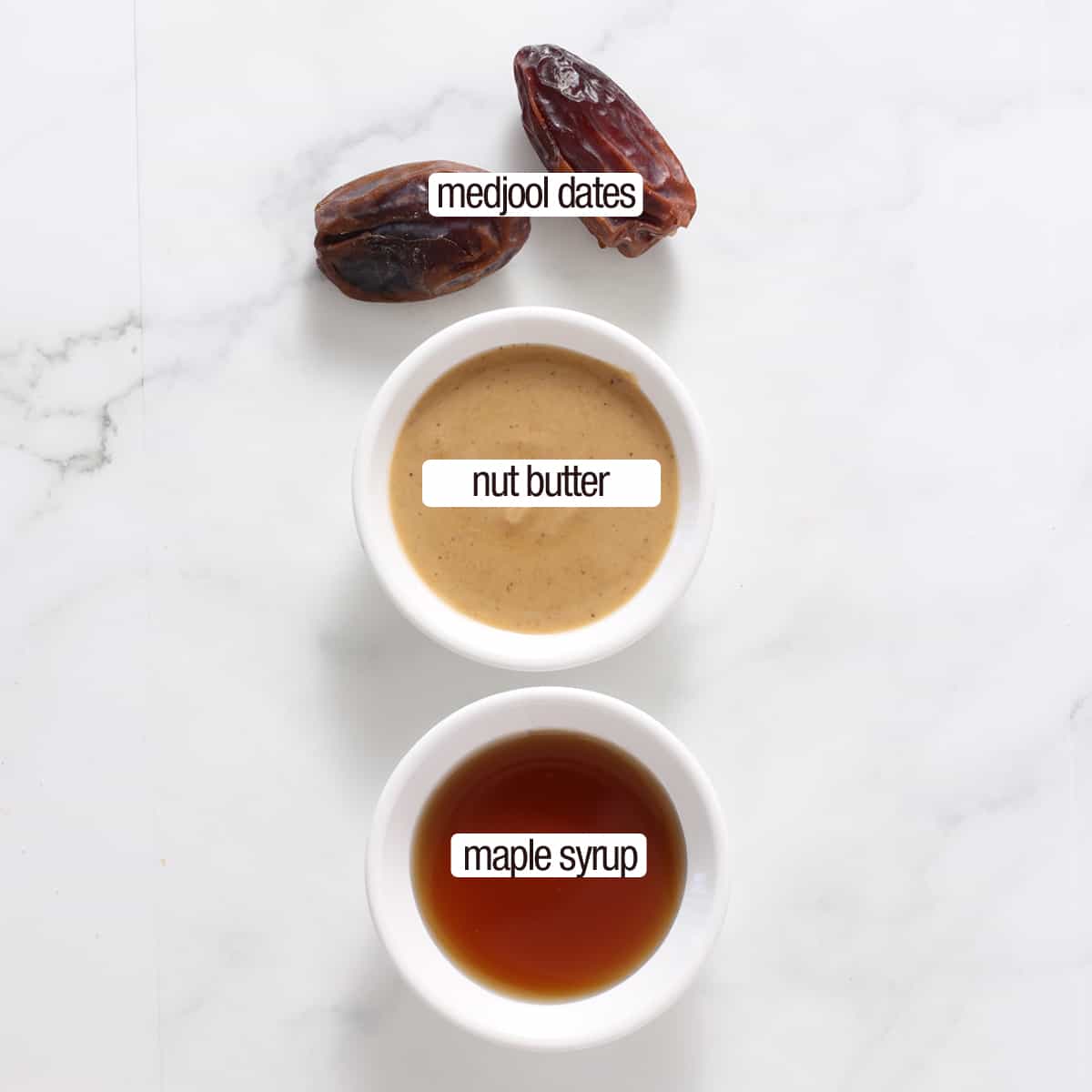 overhead of bowls of nut butter,maple syrup and dates