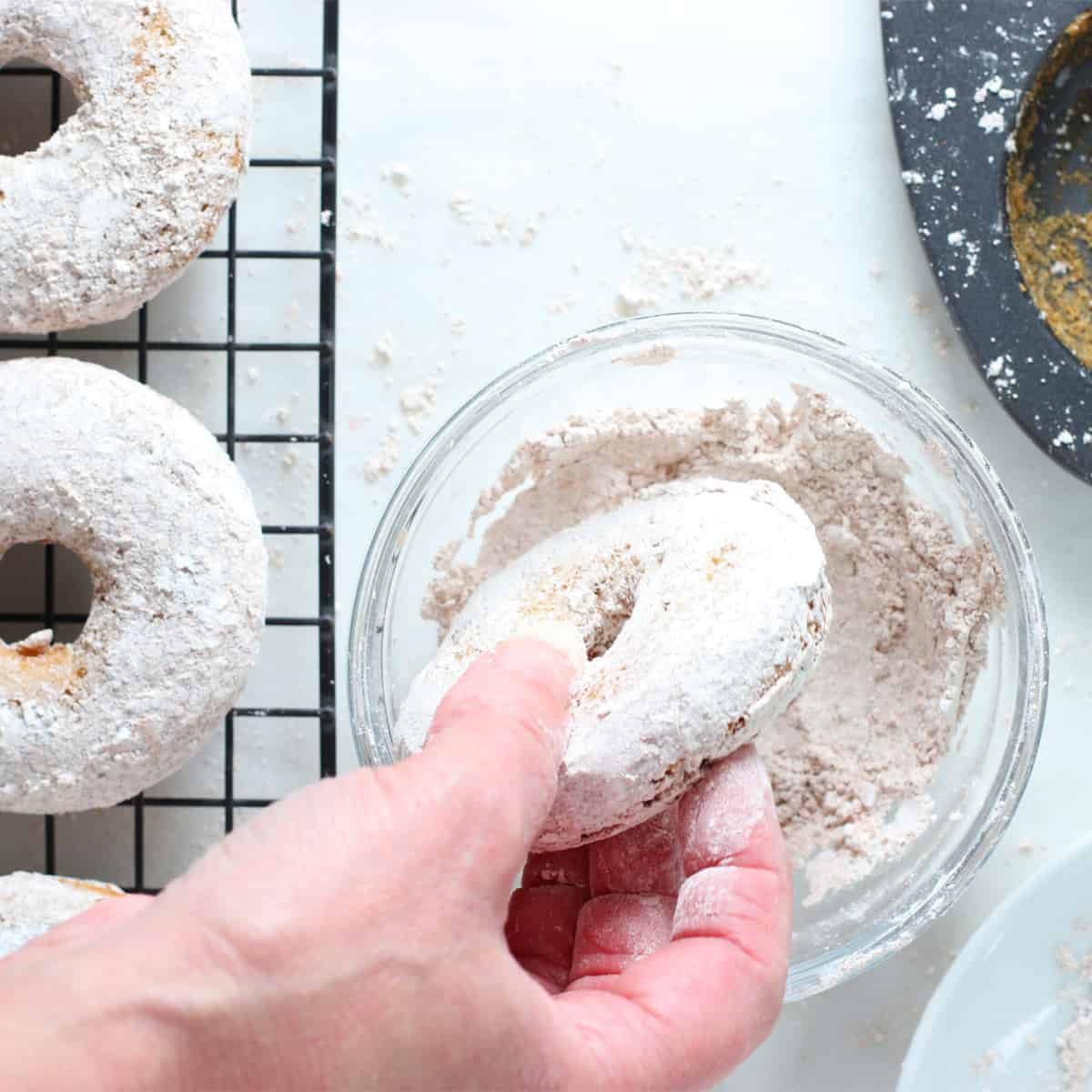 dropping a donut into powdered sugar.
