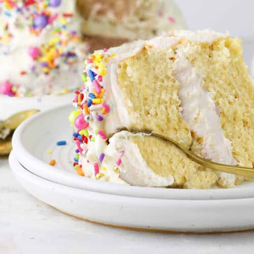 a slice of yellow vanilla cake with white frosting with rainbow sprinkles