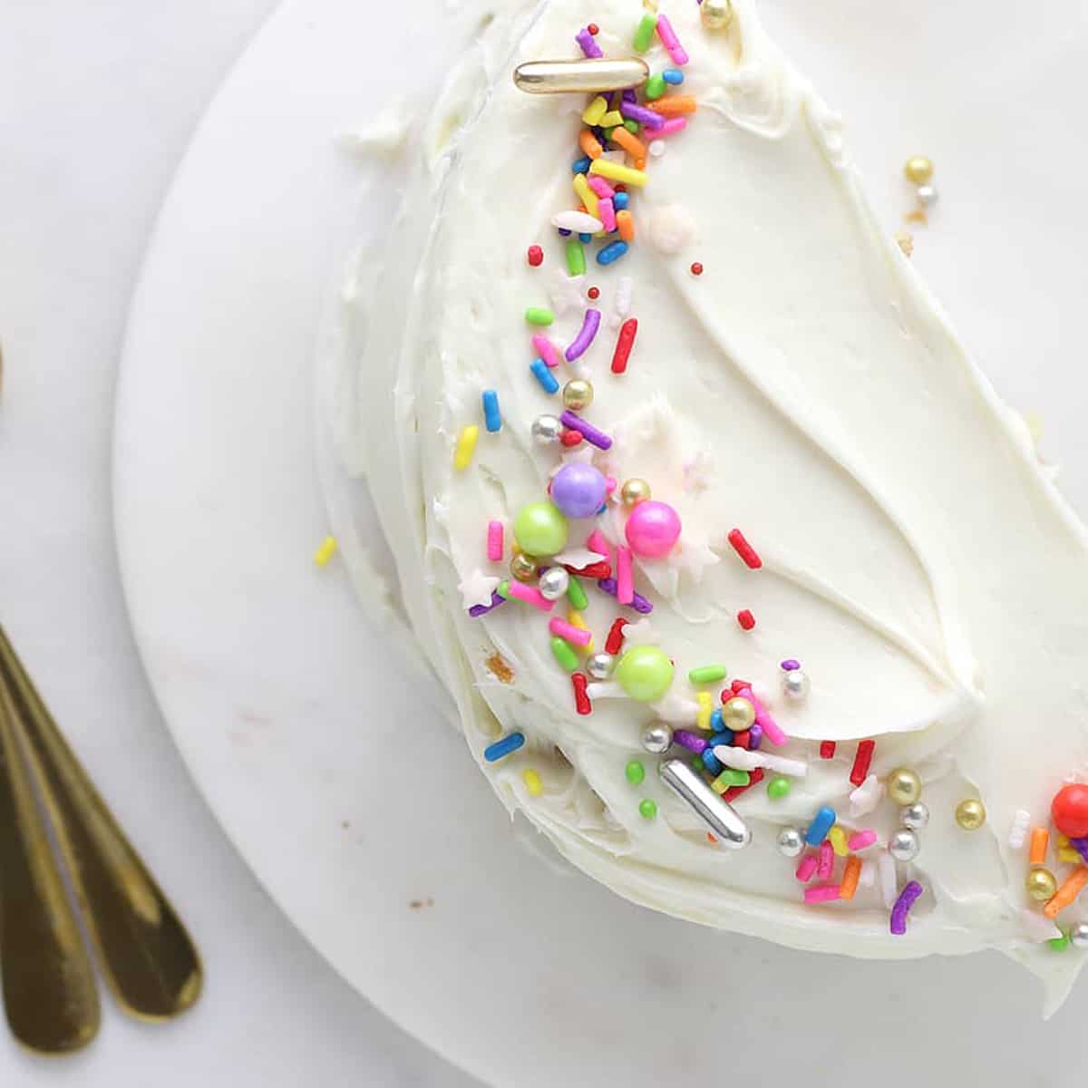 overhead of half yellow vanilla cake with white frosting with rainbow sprinkles