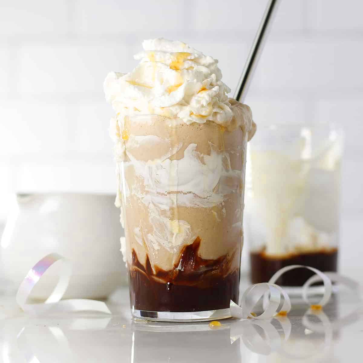 a straight on view of a caramel frappe with cream on top and strraw