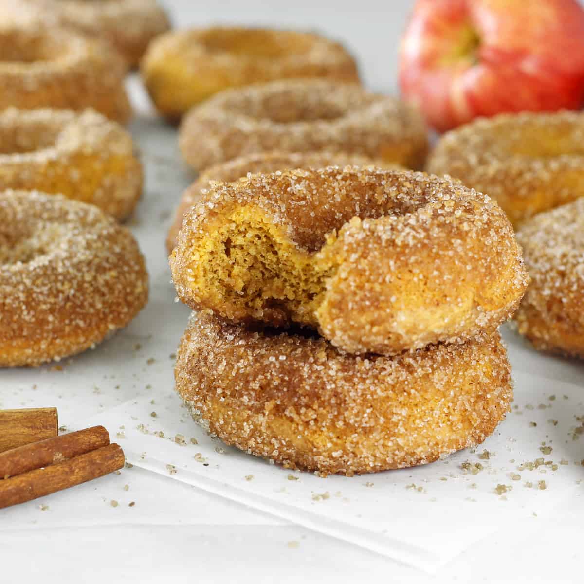 Apple Cider Donuts stacked on a parchment paper on a table with a bite out
