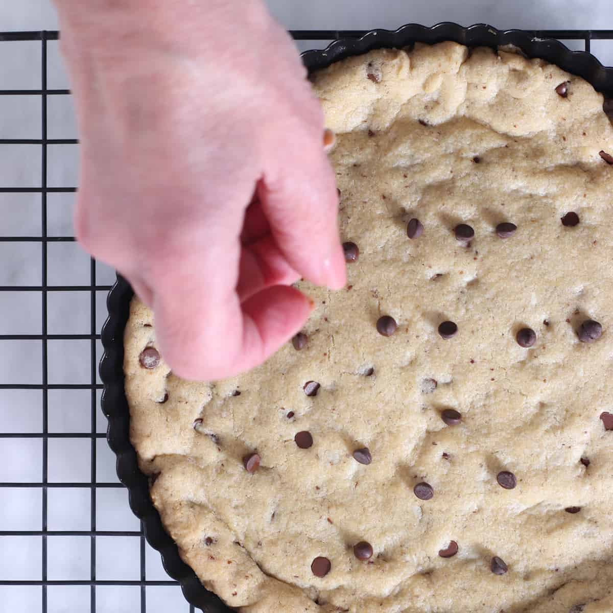 hot cookie cake with hand putting chocolate chips on top