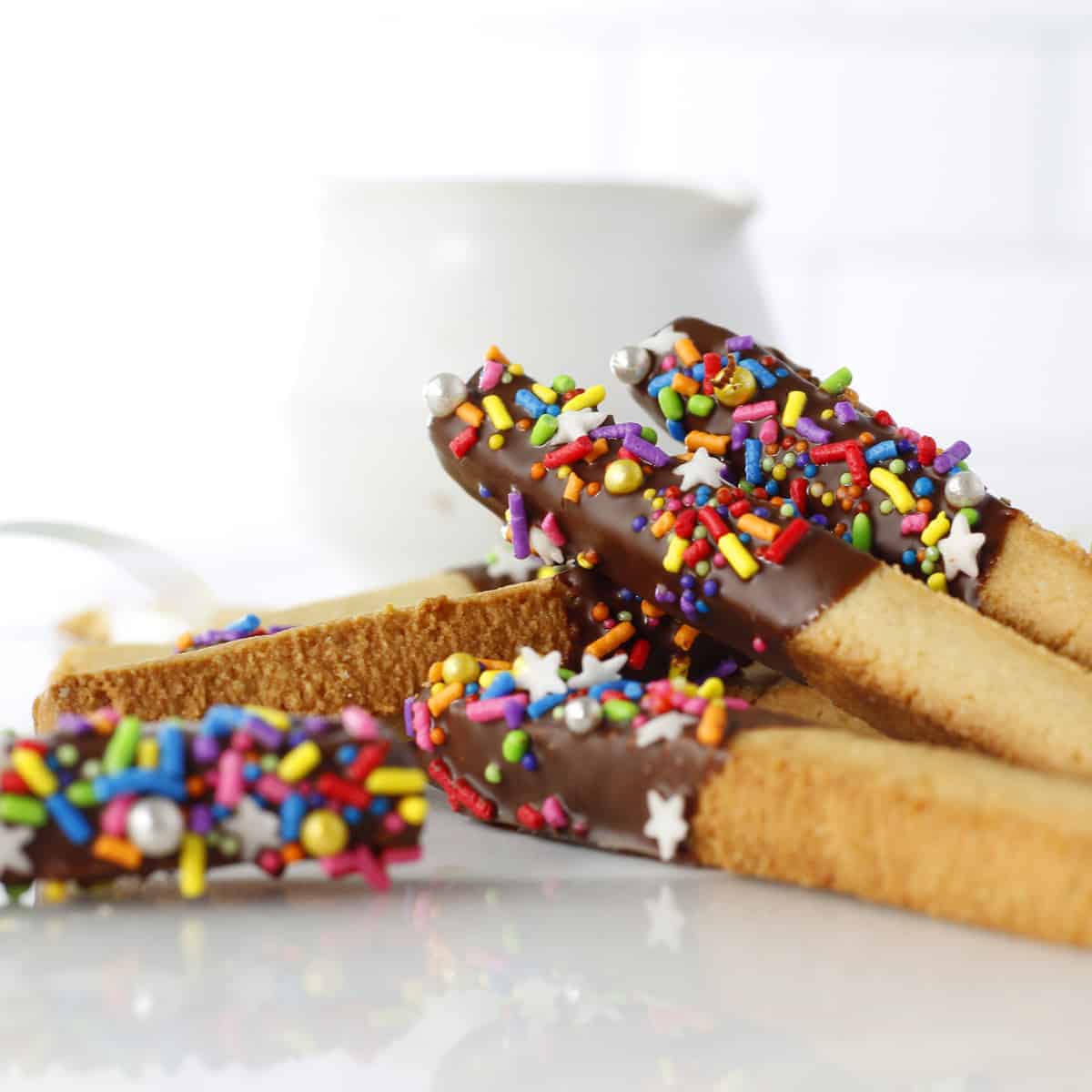 a pile of cookie sticks with a coating and sprinkles.