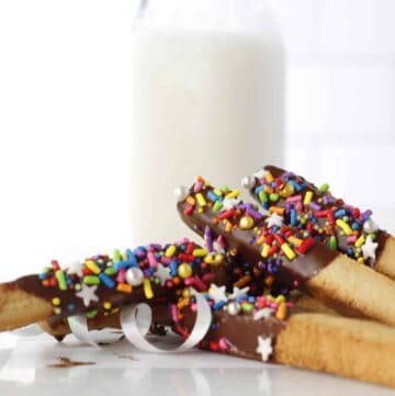 a pile of cookie sticks with milk behind it.