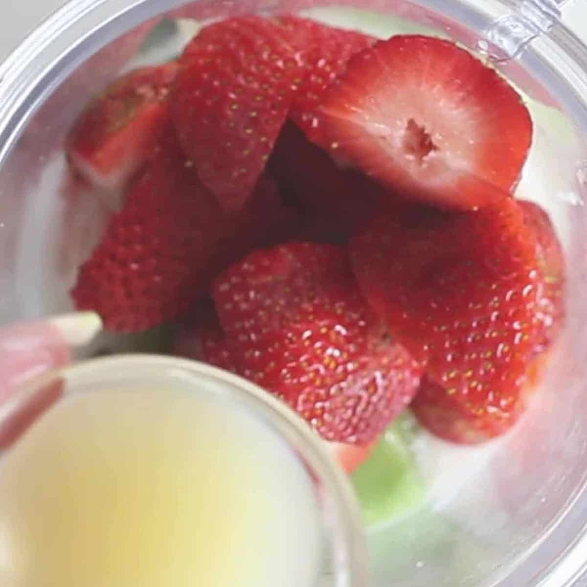 strawberries in a blender and a cup of lemon juice.