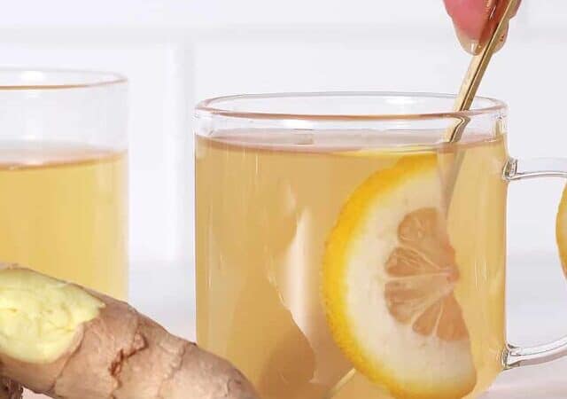 a cup of ginger tea being stirred with ginger root next to it