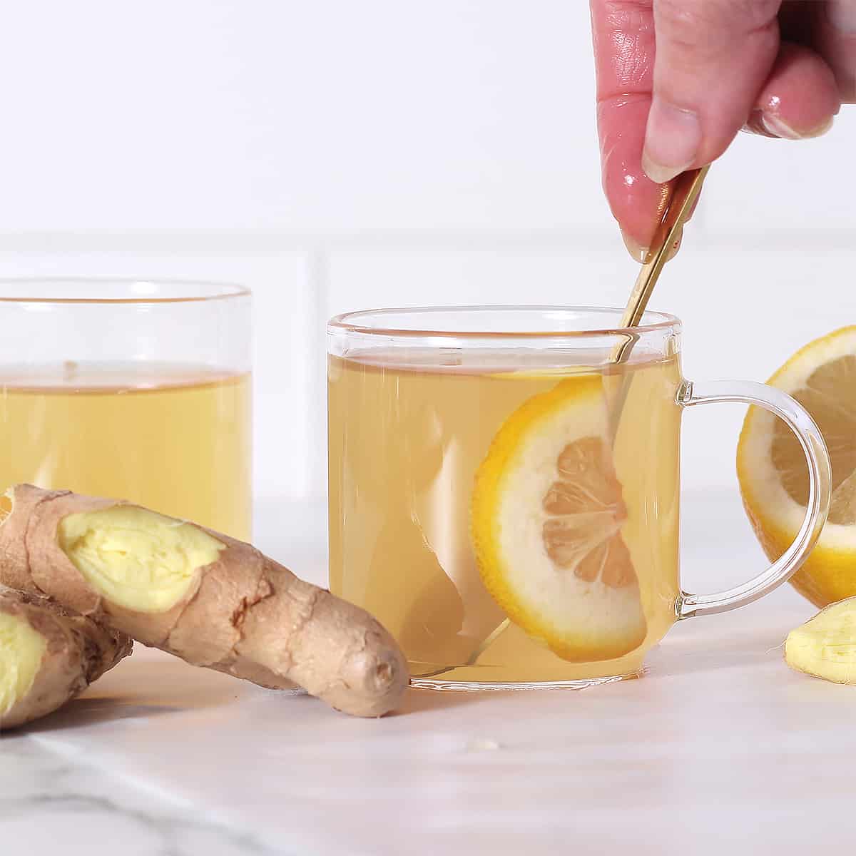 a cup of ginger tea being stirred with ginger root next to it