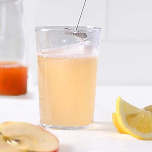frothed apple cider vinegar drink in glass with apple slices and lemons