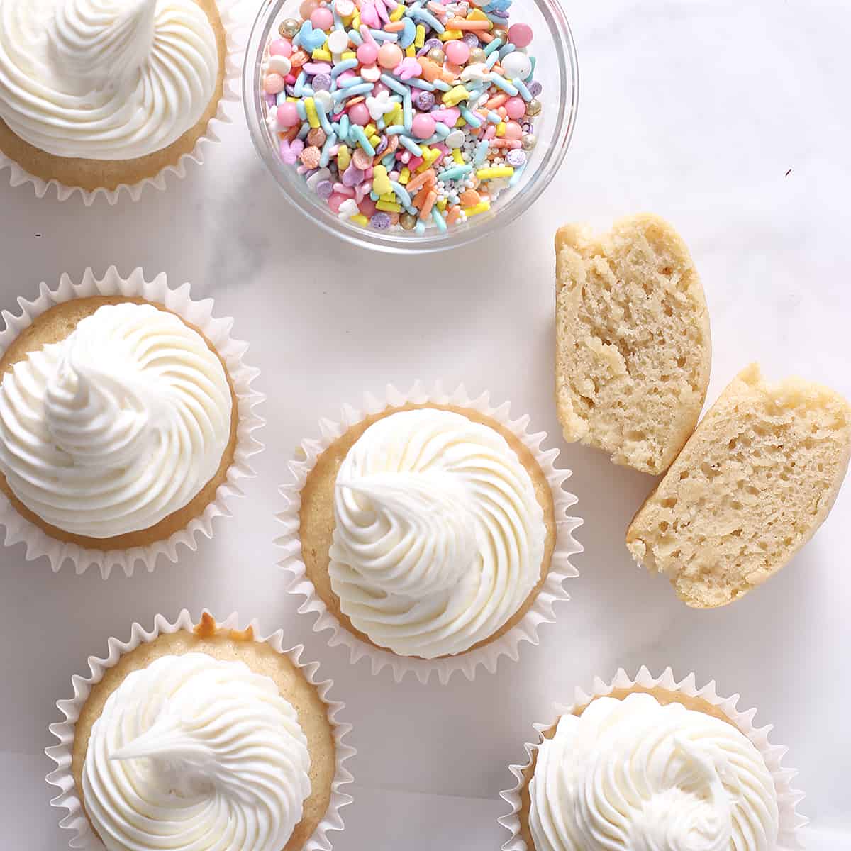 overhead of vanilla frosted cupcakes and a bowl of sprinkles