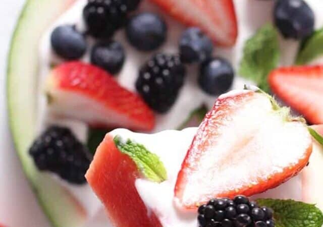 a hand holding a slice of watermelon pizza