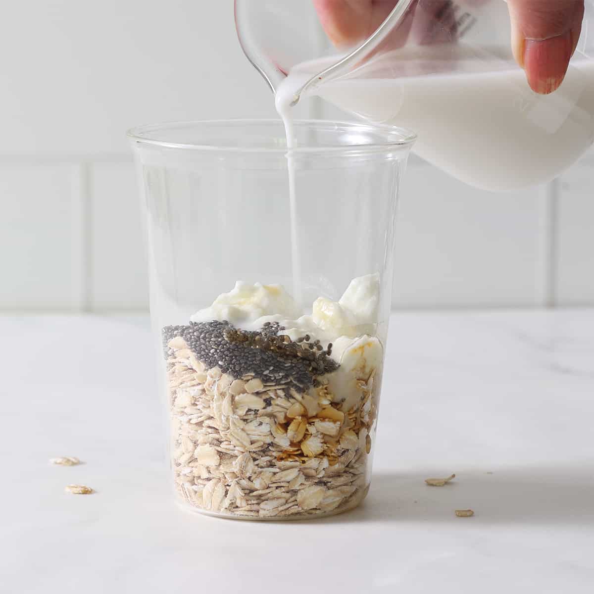 adding ingredients for overnight oats to a glass.