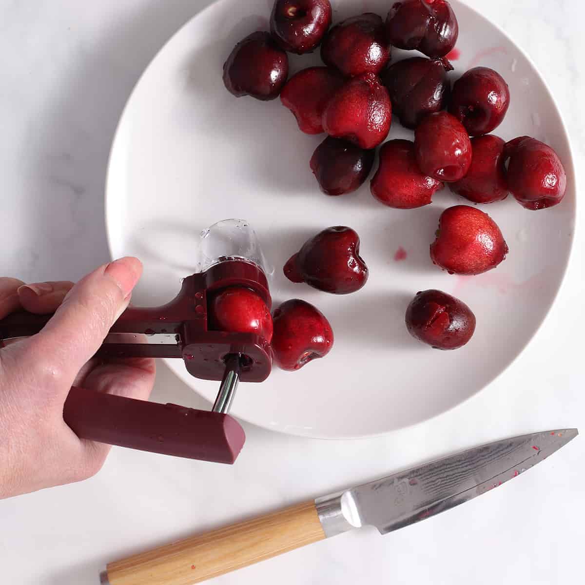 cherry pitter held by hand over a dish of cherries