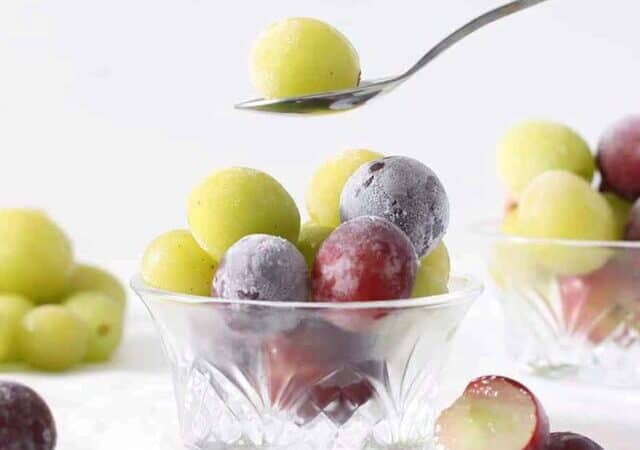 frozen grapes in a bowl with a spoon holding one above it.