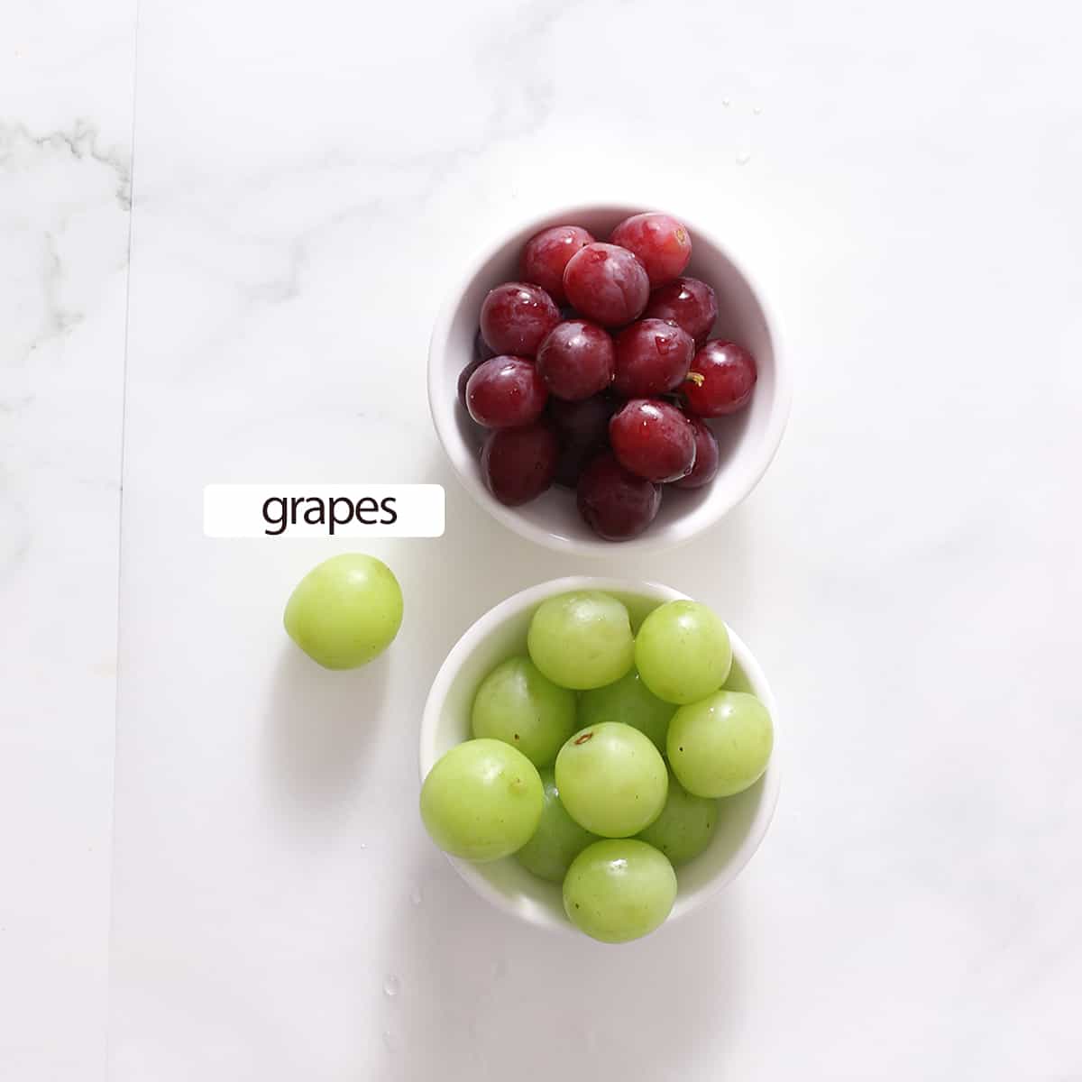 overhead shot of ingredients for frozen grapes, two bowls of grapes.