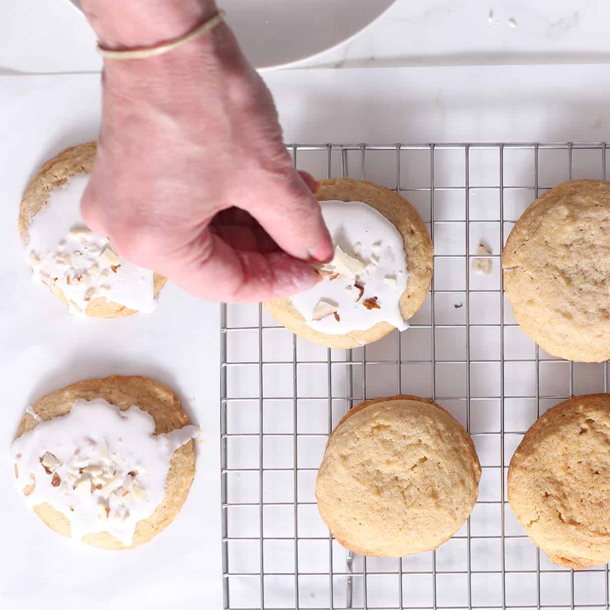 frosted almond sugar cookies with a hand putting on crushed almonds.