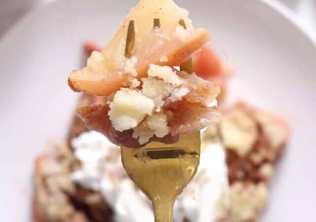 apple crisp on a dish with cinnamon sticks and an apple and fork.