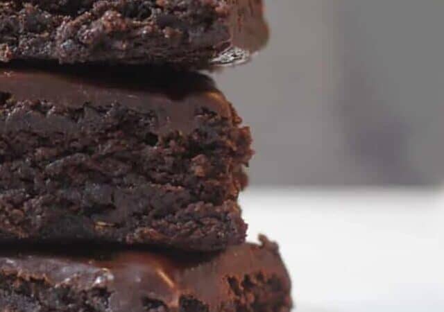 a close up of three fudge brownies on a white dish.