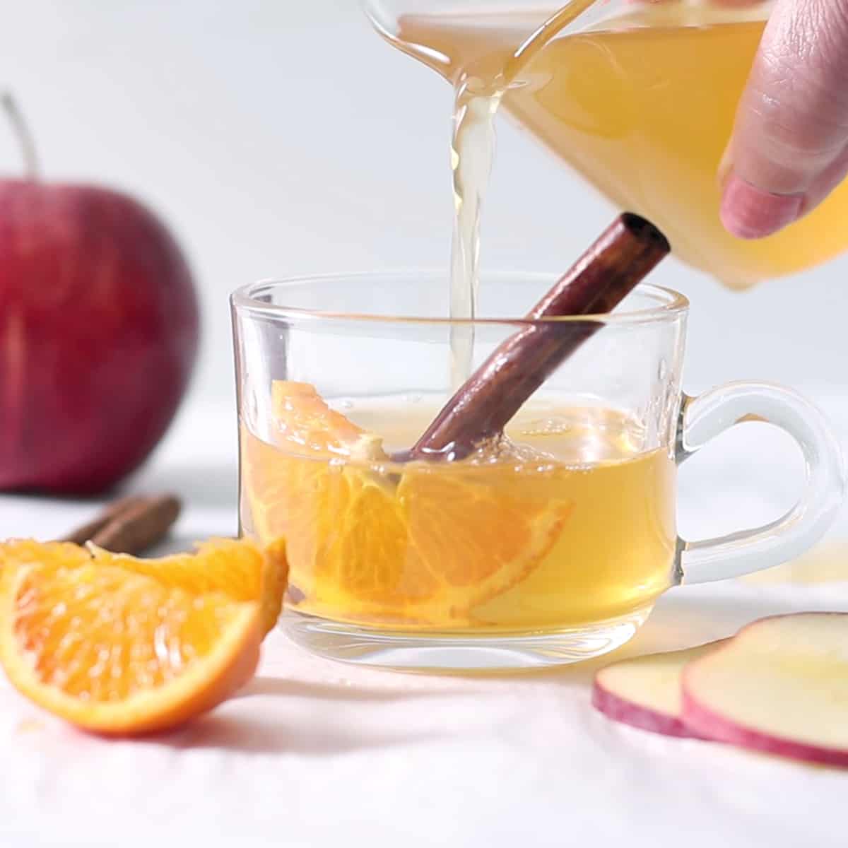 pouring apple cider that has been spiced, with a cinnamon stick.