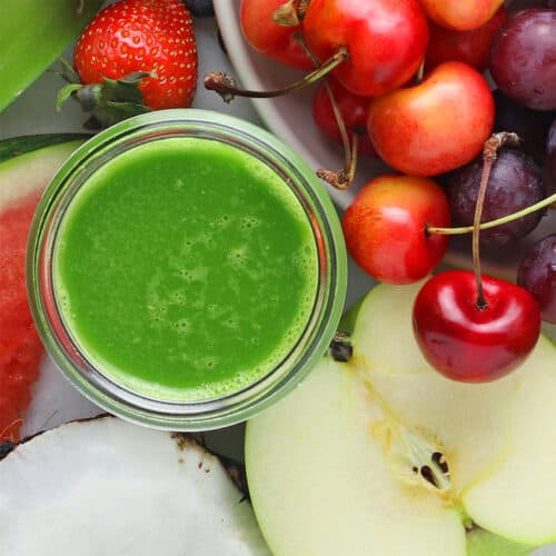 green smoothie in glass surrounded by fruit.
