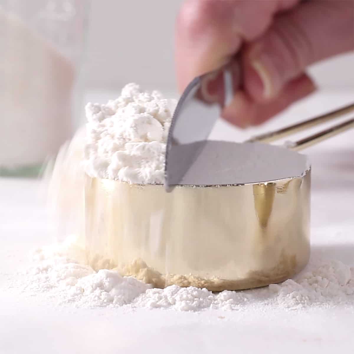 a knife is used to level off the flour in a measuring cup.