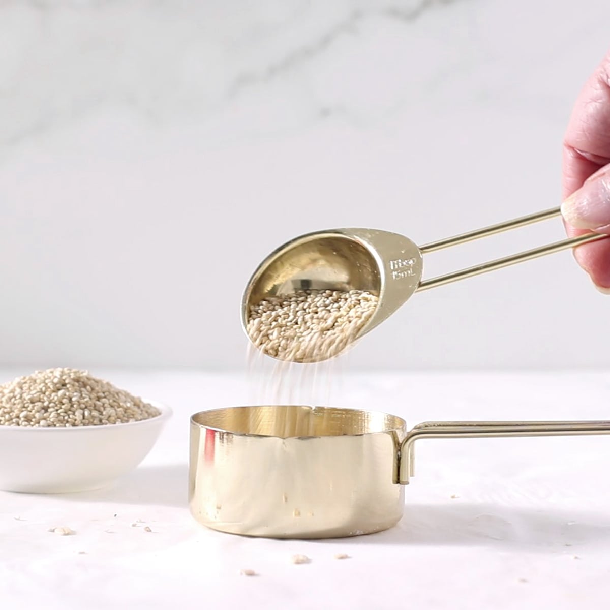 pouring quinoa into a ½ cup with a tablespoon.